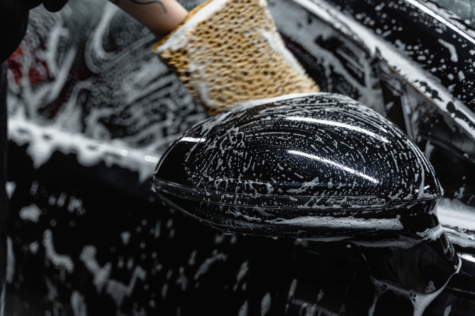 Hand washing a car mirror with a wash mitt